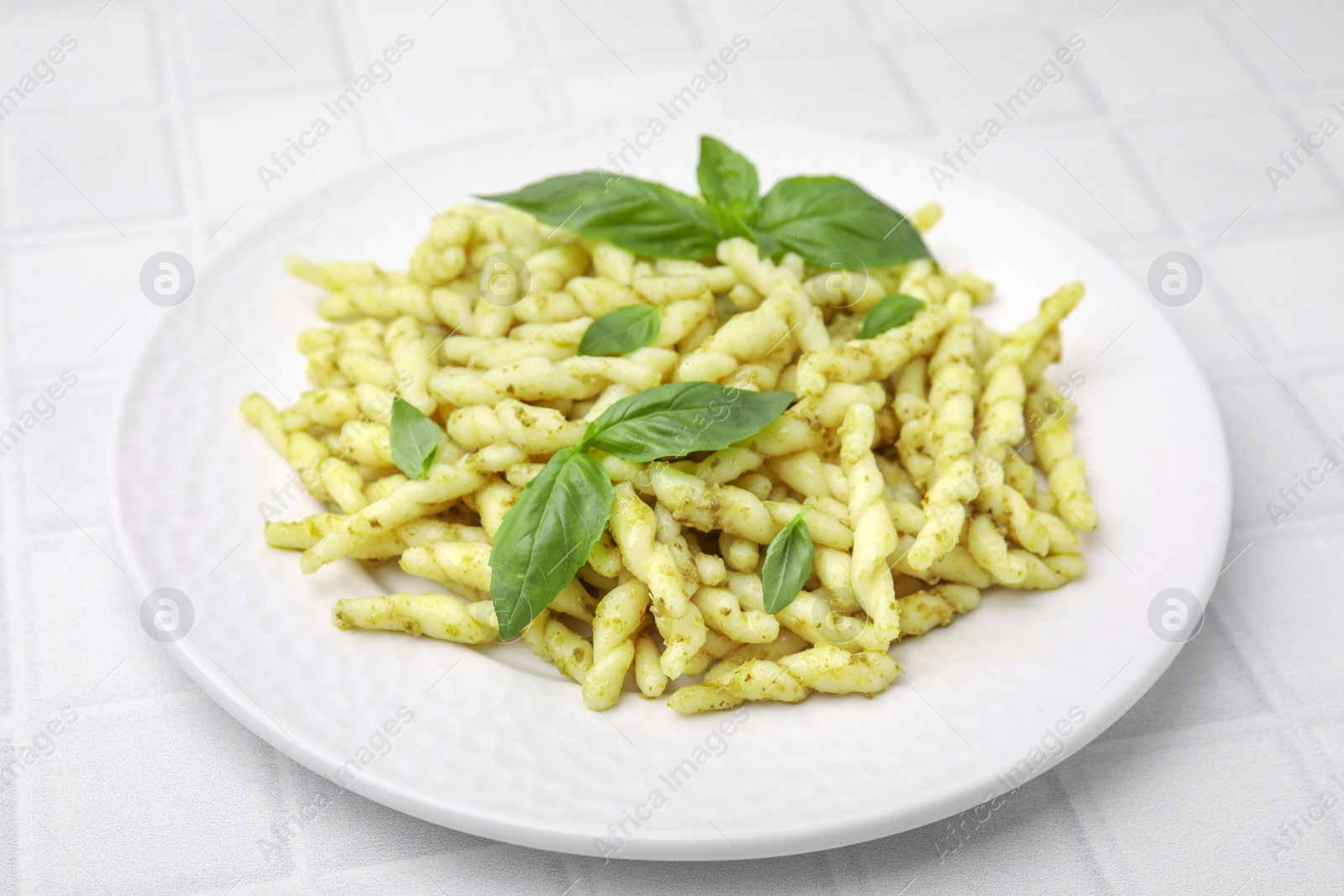 Photo of Plate of delicious trofie pasta with pesto sauce and basil leaves on white tiled table