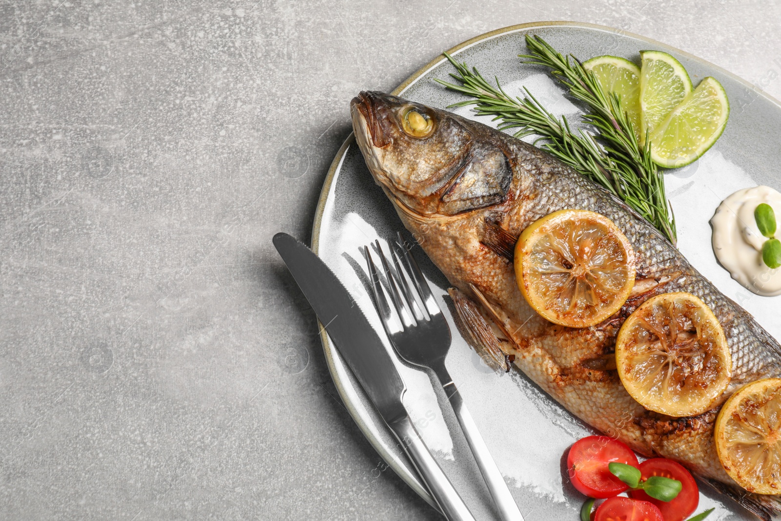 Photo of Delicious baked sea bass fish served with lemon, rosemary and sauce on light grey table, top view. Space for text