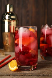 Photo of Tasty cranberry cocktail with ice cubes and orange in glasses on wooden table