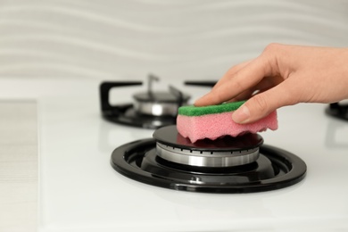 Photo of Woman cleaning gas stove with sponge, closeup