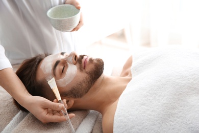 Cosmetologist applying mask on client's face in spa salon