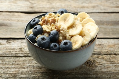 Photo of Tasty oatmeal with banana, blueberries and walnuts served in bowl on wooden table