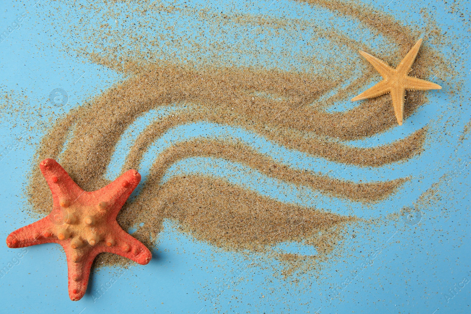 Photo of Beautiful sea stars and sand on light blue background, flat lay