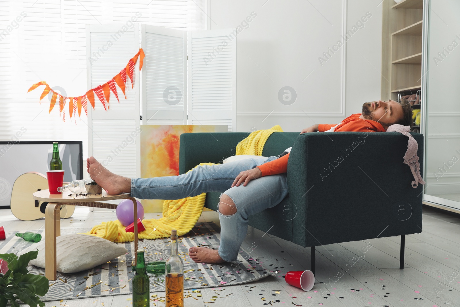 Photo of Young man sleeping on sofa in messy room after party