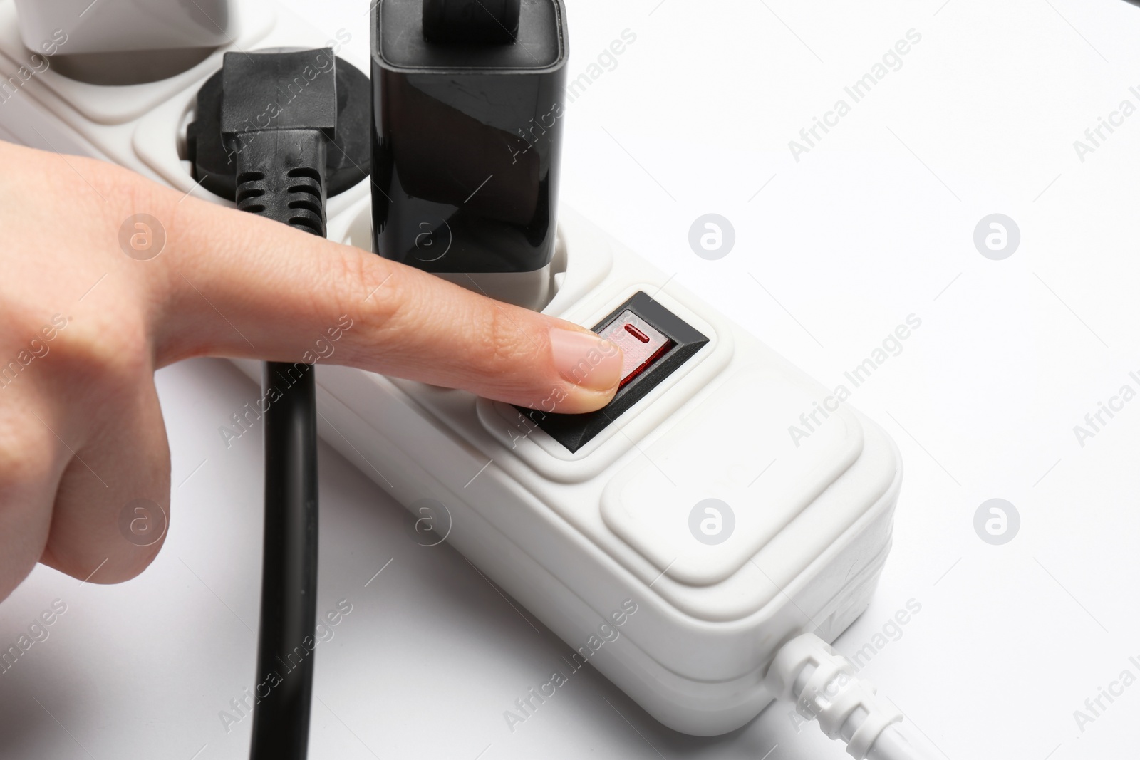 Photo of Woman pressing power button of extension cord on white background, closeup. Electrician's professional equipment