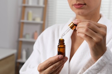 Photo of Woman with bottle of cosmetic serum and dropper indoors, closeup