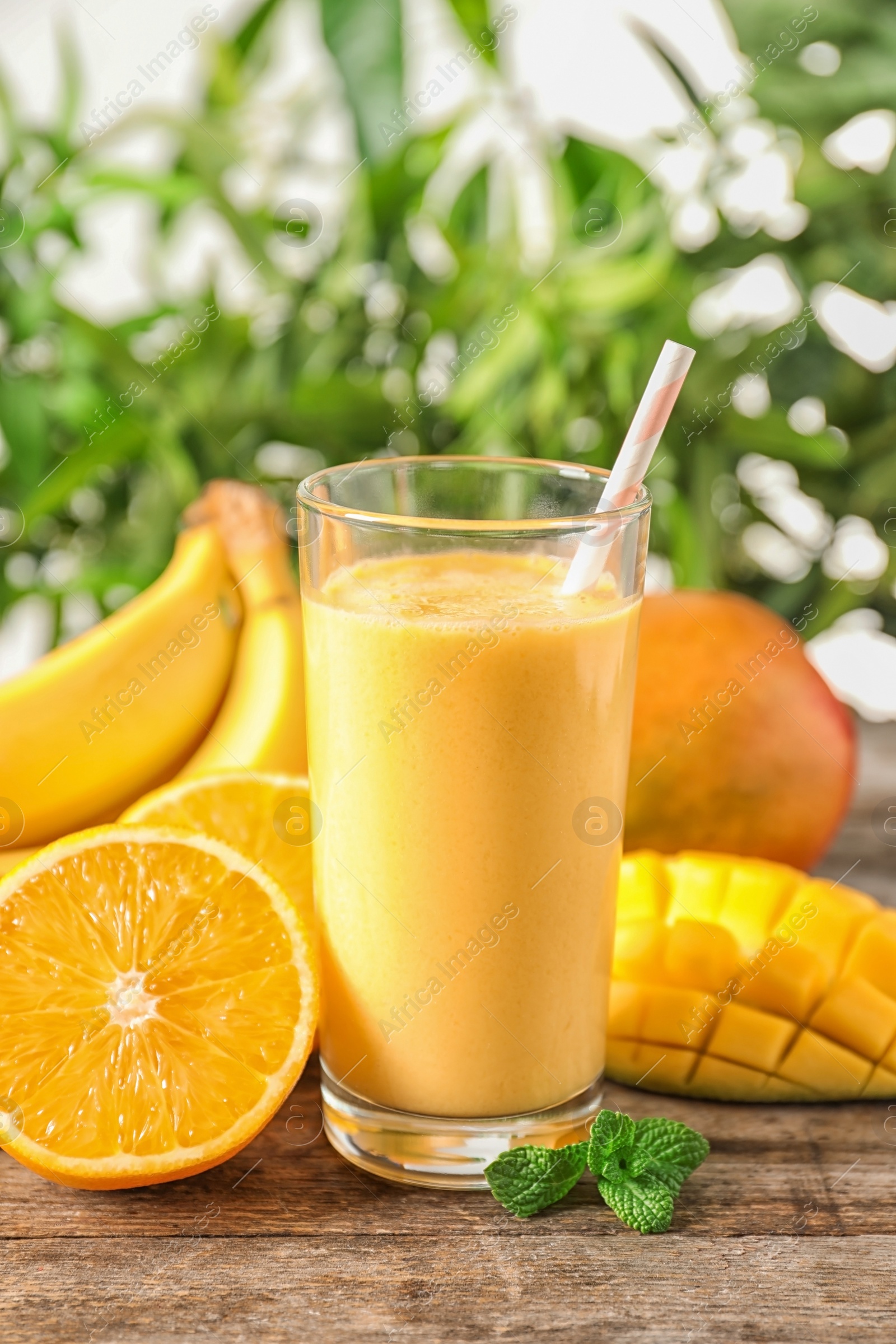 Photo of Fresh tropical drink with ripe mango, orange and banana on wooden table against blurred background