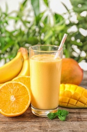 Fresh tropical drink with ripe mango, orange and banana on wooden table against blurred background