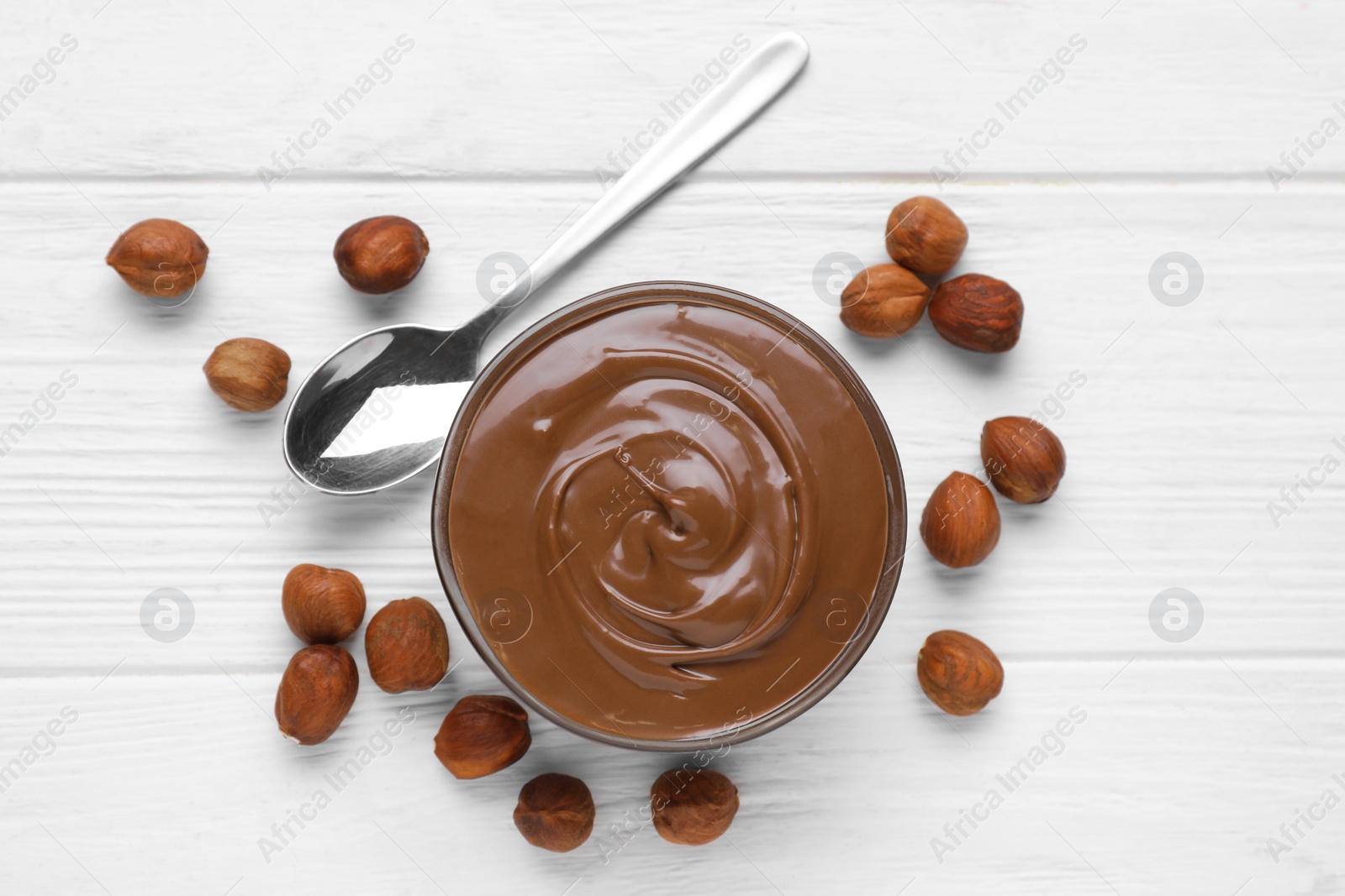 Photo of Bowl with delicious chocolate paste and nuts on white wooden table, flat lay