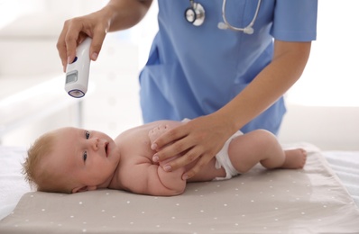 Photo of Doctor measuring temperature of little baby with non-contact thermometer in clinic, closeup. Health care