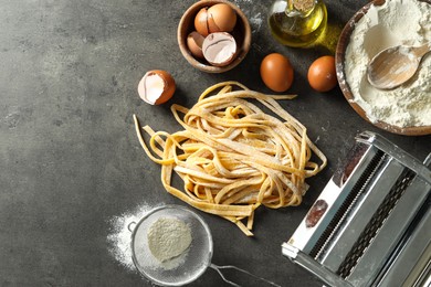Photo of Homemade pasta, maker and ingredients on dark grey table, flat lay