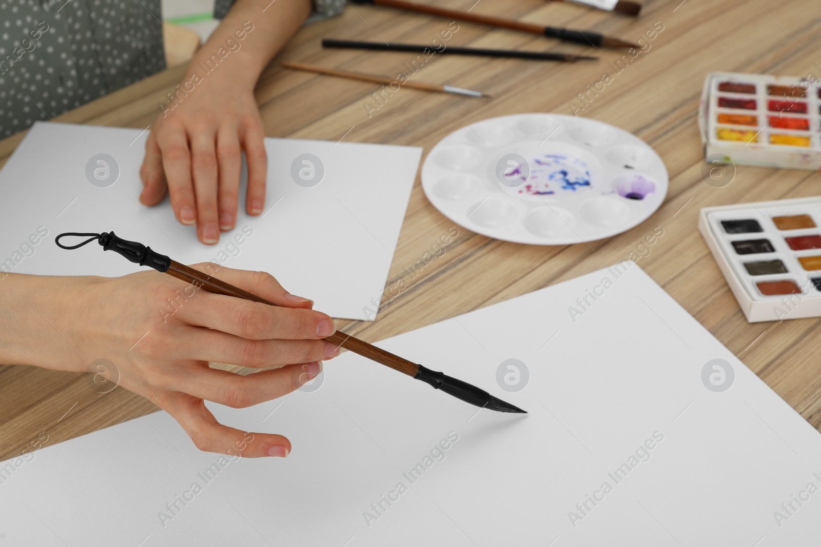 Photo of Woman painting with watercolor on blank paper at wooden table, closeup