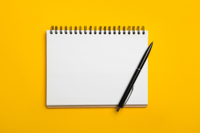 Photo of Open notebook and pen on yellow background, top view