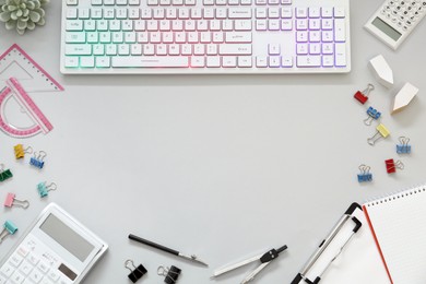 Photo of Frame of modern RGB keyboard and office stationery on light grey background, flat lay. Space for text