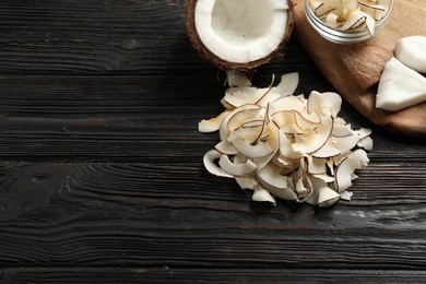 Photo of Pile of tasty coconut chips on black wooden table, above view. Space for text