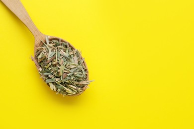 Photo of Wooden spoon with aromatic dried lemongrass on yellow background, top view. Space for text