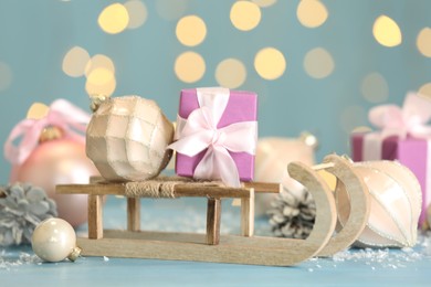 Photo of Wooden sleigh with gift boxes and Christmas ornaments on light blue table against blurred lights