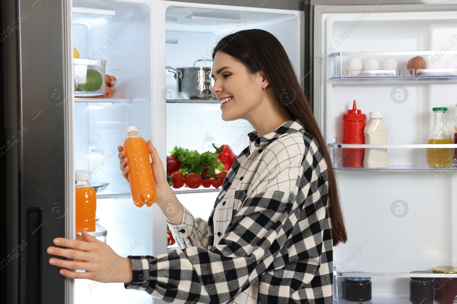 Photo of Young woman taking bottle of juice out of refrigerator
