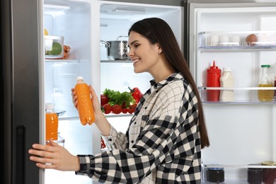 Young woman taking bottle of juice out of refrigerator