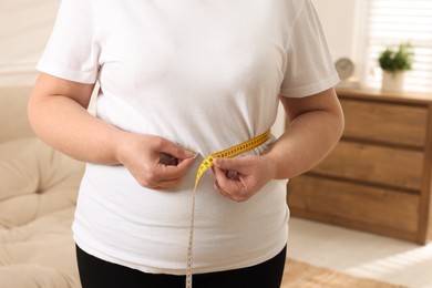 Photo of Overweight woman measuring waist with tape at home, closeup