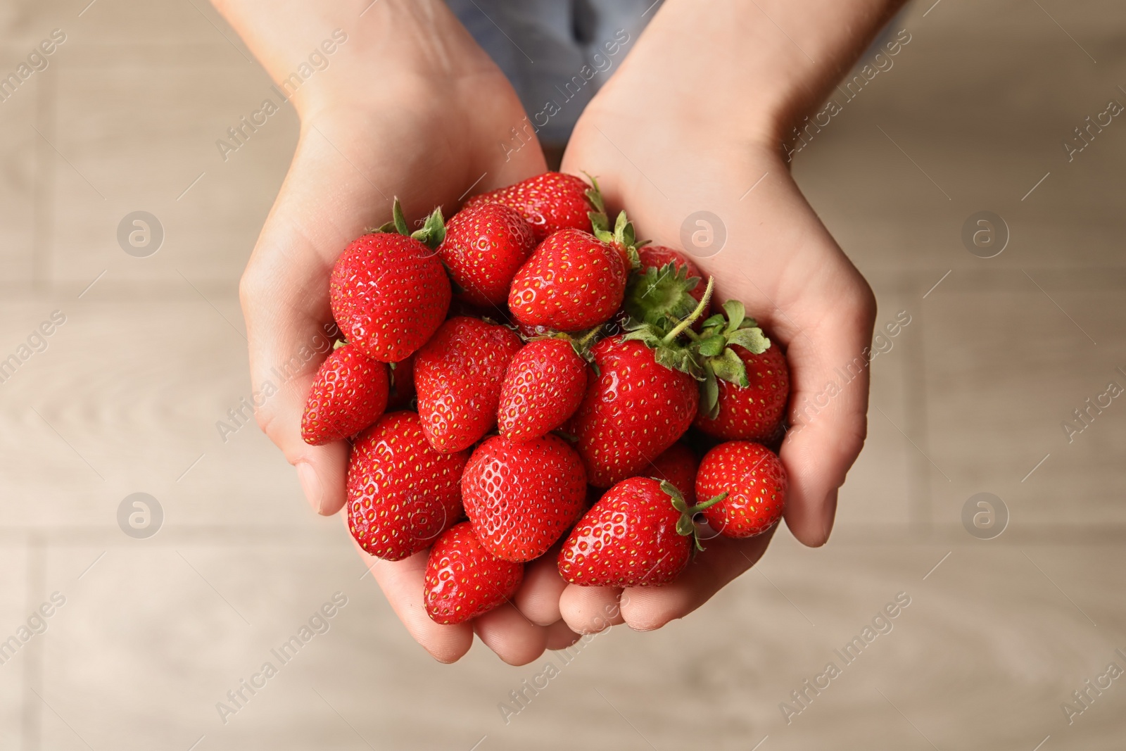 Photo of Young woman holding fresh ripe strawberries on light background, top view