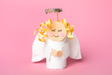 Toy angel made of toilet paper hub on pink background