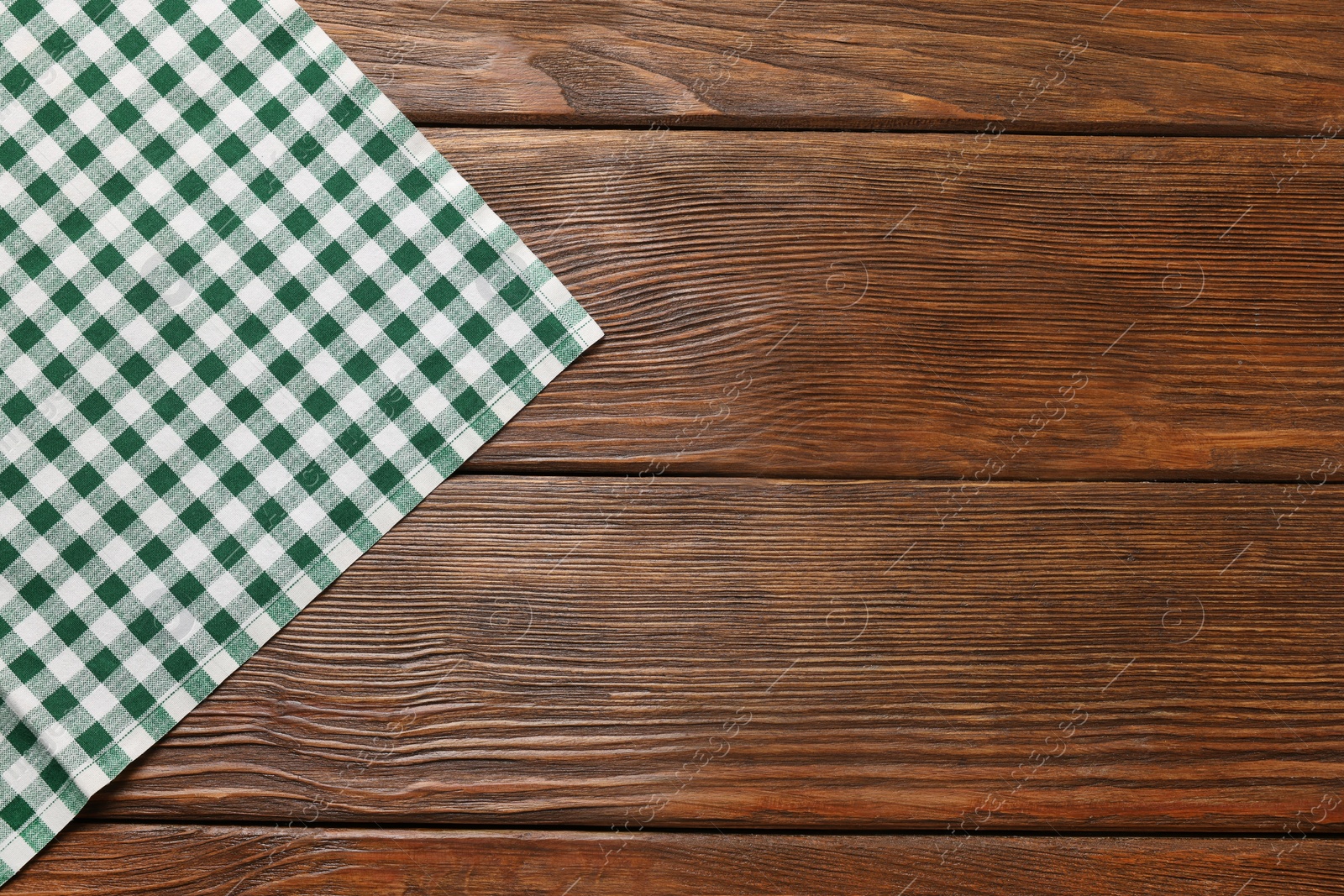 Photo of Green checkered tablecloth on wooden table, top view. Space for text