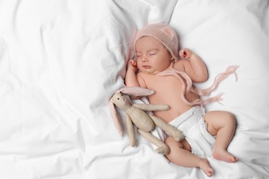 Photo of Cute little baby with toy bunny sleeping on soft bed, top view. Space for text