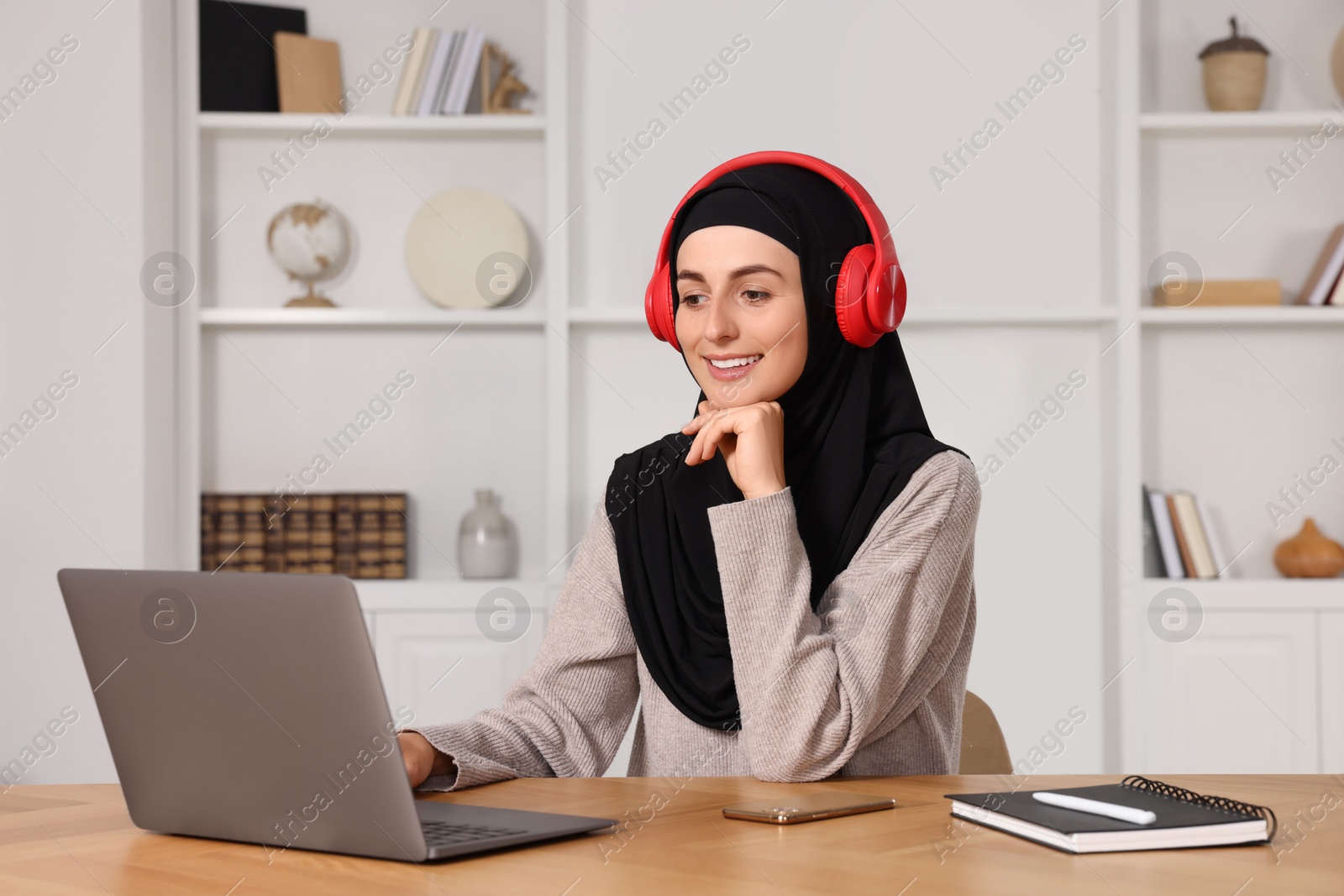 Photo of Muslim woman in hijab using laptop at wooden table in room