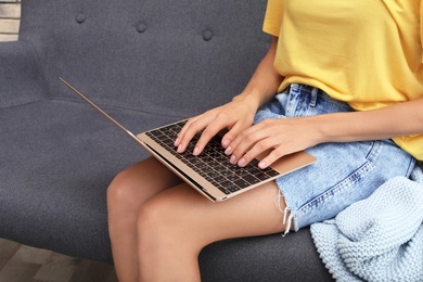 Young woman with modern laptop sitting on sofa at home, closeup