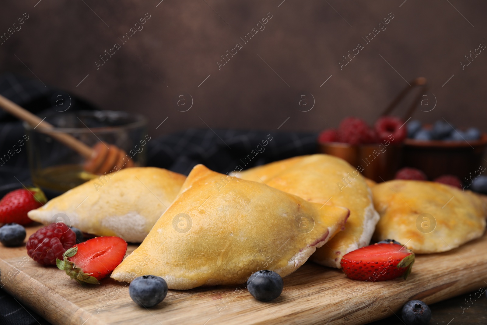 Photo of Wooden board with delicious samosas and berries on table, closeup