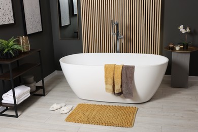Photo of Stylish bathroom interior with bath tub, houseplants and soft yellow mat