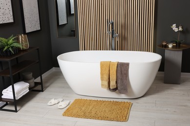 Stylish bathroom interior with bath tub, houseplants and soft yellow mat