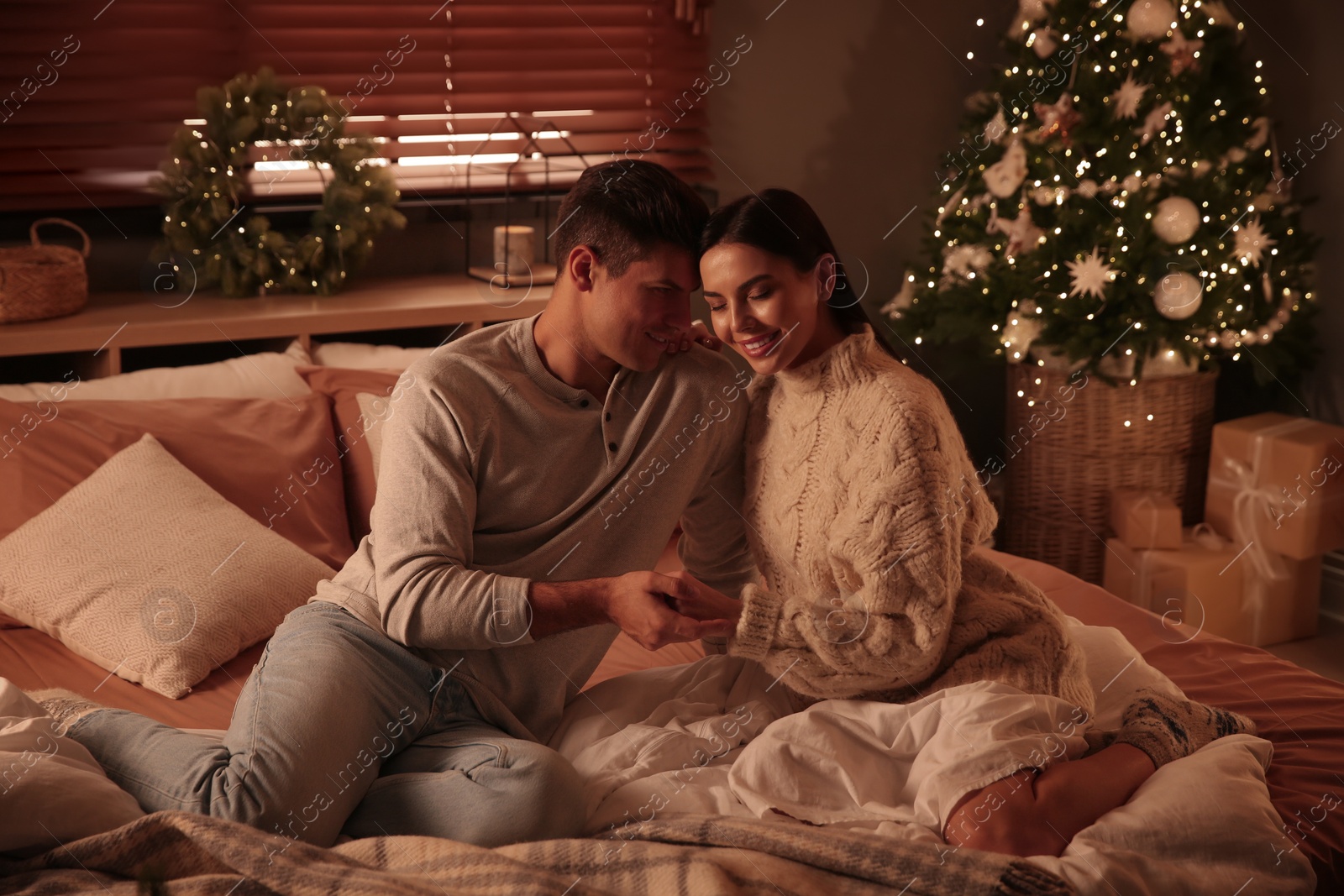 Photo of Happy couple sitting on bed in festively decorated room. Christmas celebration
