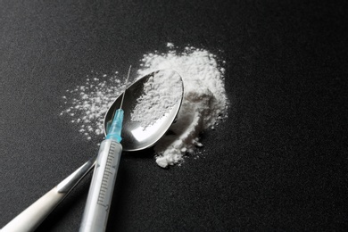 Photo of Spoon with cocaine powder and syringe on dark background. Space for text