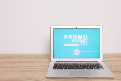 Photo of Laptop with activated promo code on wooden table near white wall. Space for text