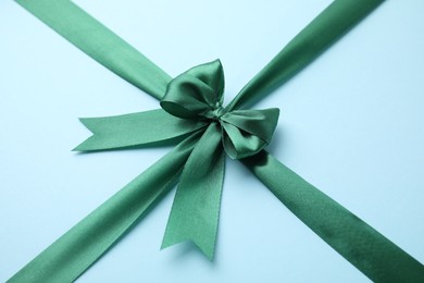 Green satin ribbon with bow on light blue background, closeup