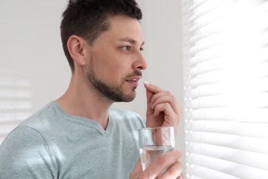 Man with glass of water taking pill at home