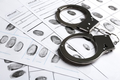 Handcuffs and fingerprint record sheets, closeup. Criminal investigation