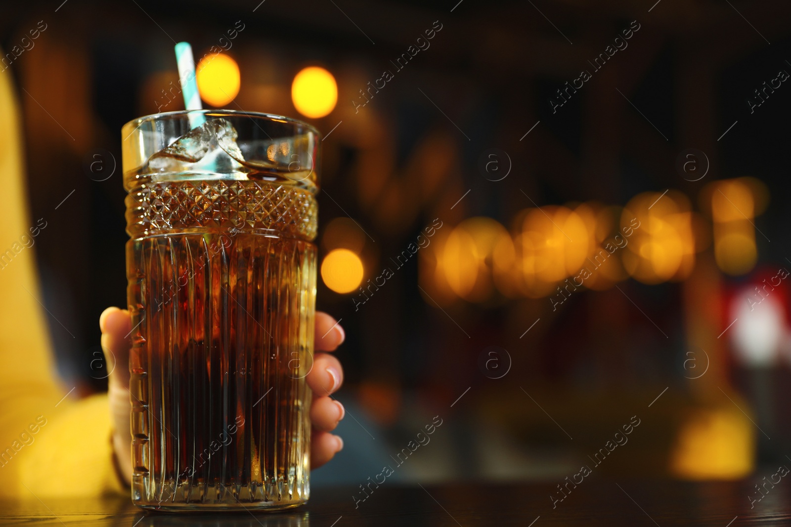 Photo of Woman with glass of refreshing cola at table indoors, closeup. Space for text