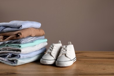 Stack of baby boy's clothes and shoes on wooden table against brown background, space for text