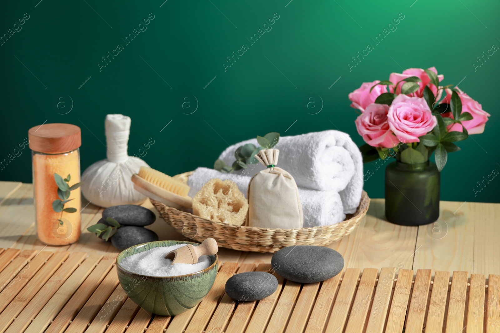Photo of Beautiful composition with sea salt, flowers and different spa products on wooden table near green wall, space for text