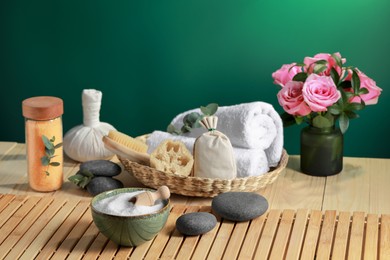 Beautiful composition with sea salt, flowers and different spa products on wooden table near green wall, space for text