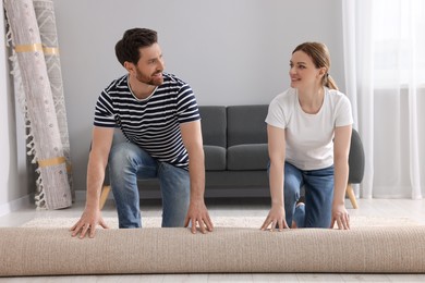 Smiling couple unrolling carpet on floor in room