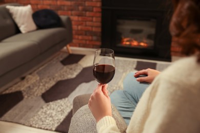 Photo of Woman with glass of wine near fireplace at home, closeup