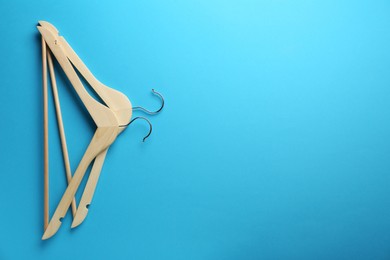 Wooden hangers on light blue background, top view. Space for text