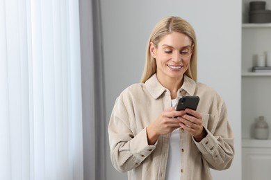 Photo of Happy woman sending message via smartphone at home, space for text