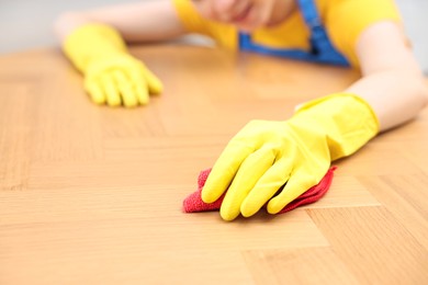 Photo of Woman cleaning wooden table with rag indoors, closeup