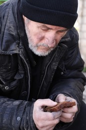 Photo of Poor homeless man holding piece of bread outdoors
