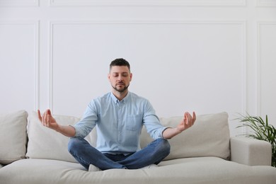 Man meditating on comfortable sofa in living room